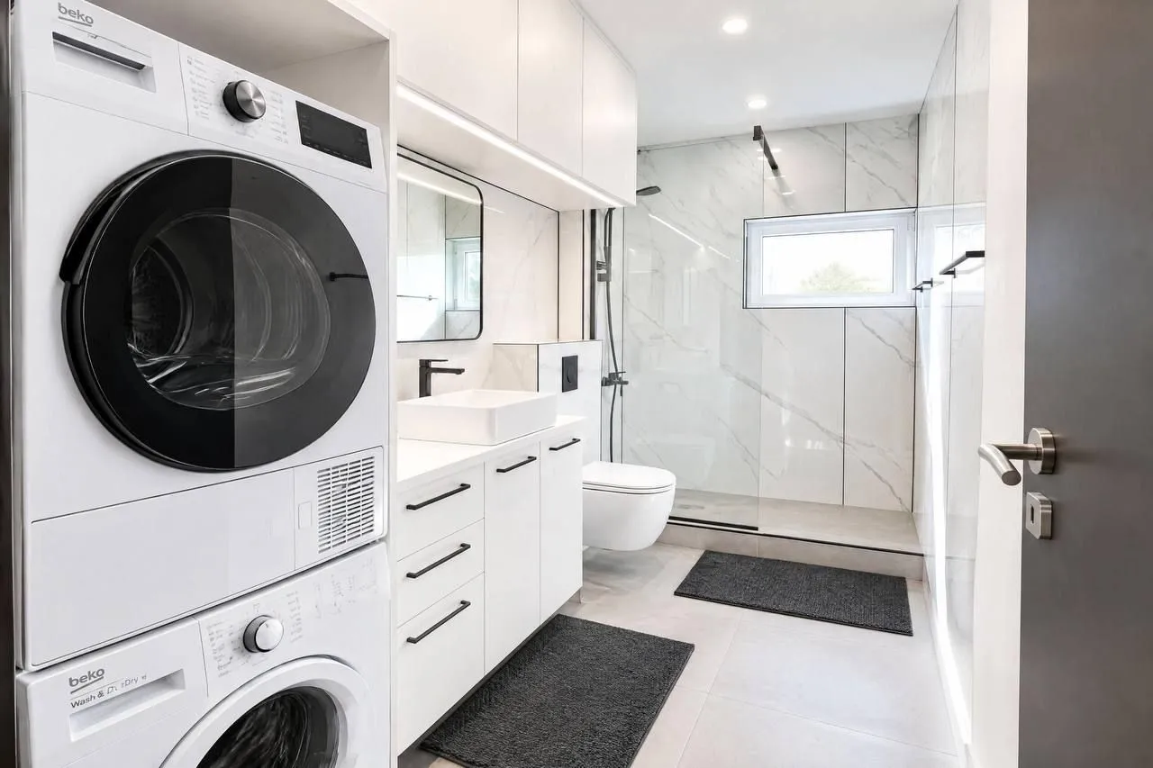 Modern bathroom with a walk-in shower, white cabinetry, and a built-in washing machine.