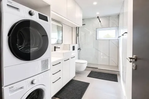 Modern bathroom with a walk-in shower, white cabinetry, and a built-in washing machine. - image 3