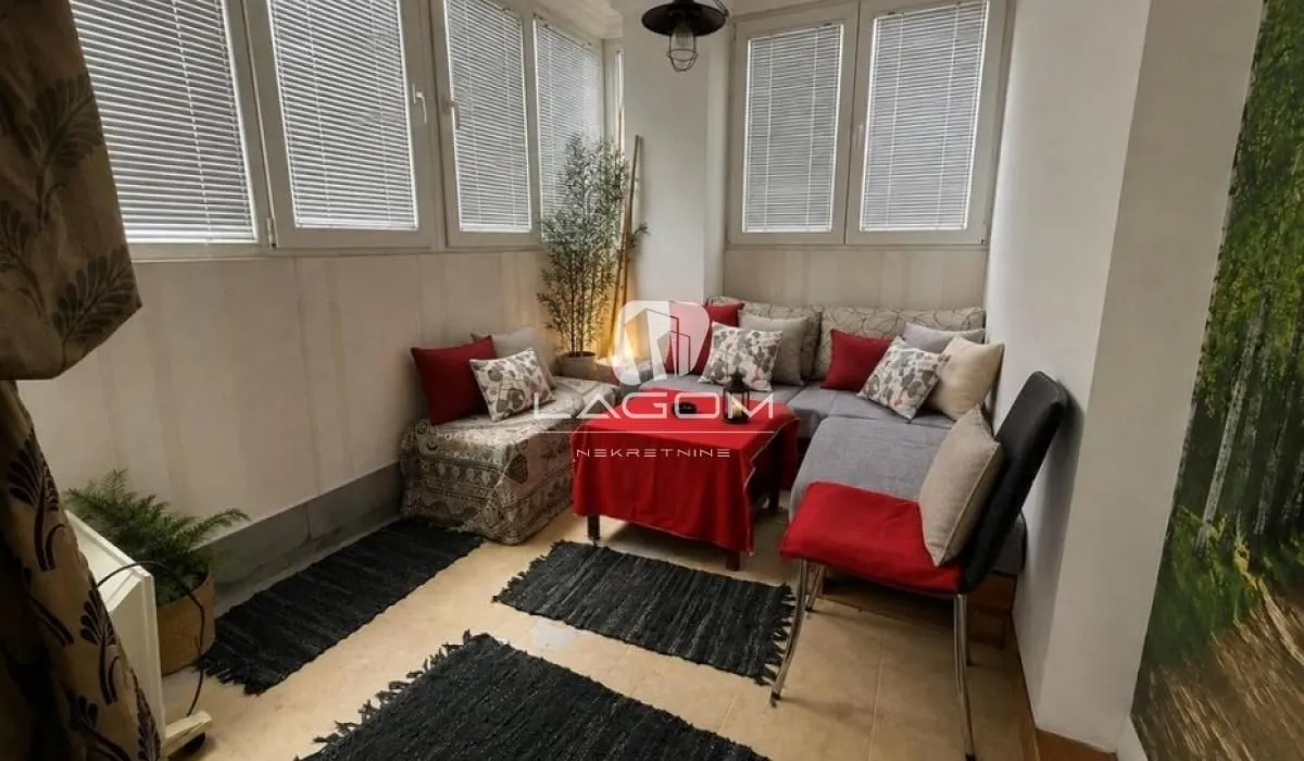 Enclosed balcony with seating furniture and windows with blinds.