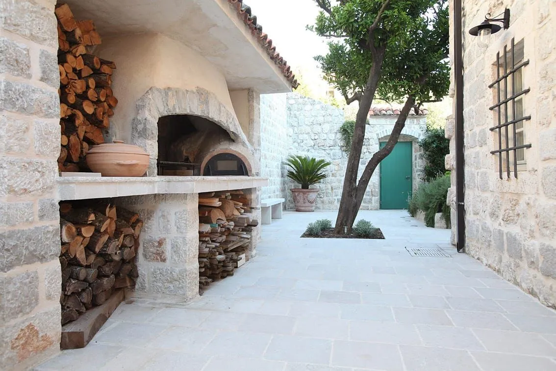 Paved courtyard with a stone barbecue, bread oven, and firewood.