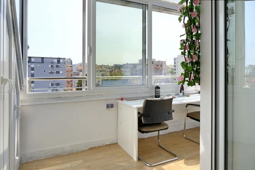 Zastakljeni balkon sa radnim stolom i pogledom na grad.