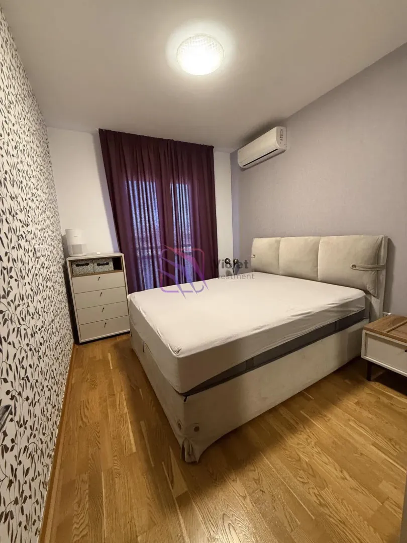 Spavaća soba sa bračnim krevetom, komodom i klima uređajem.
