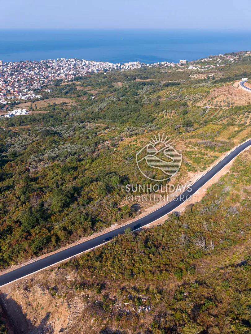 Vazdušni pogled na plac, šumoviti predio i obalu mora u daljini.