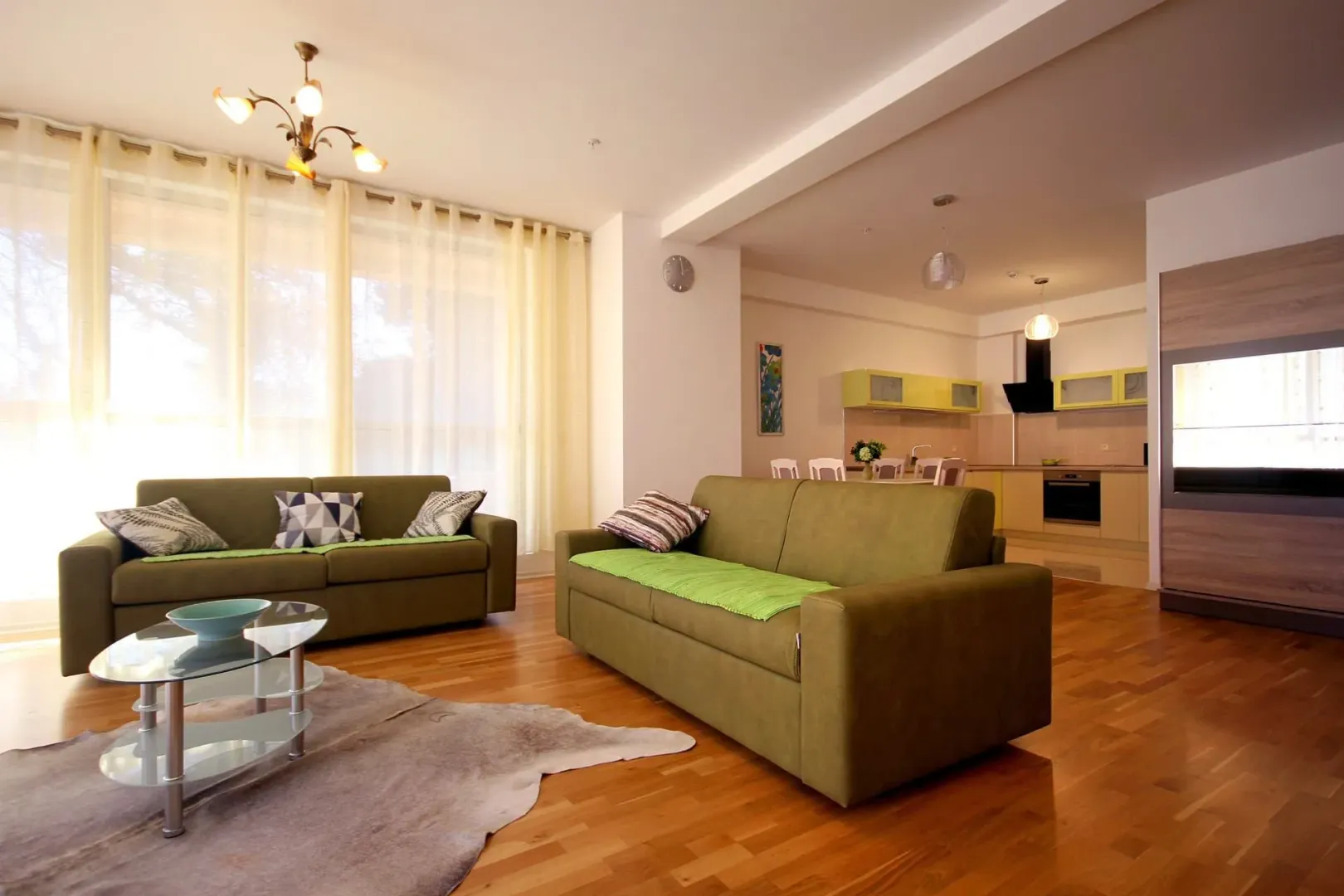 Bright open-plan living room with seating area and a kitchen in the background.