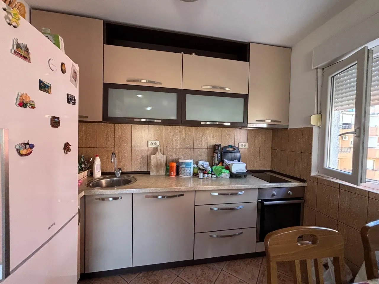Manja kuhinja sa elementima u bež boji, sudoperom, šporetom i frižiderom.