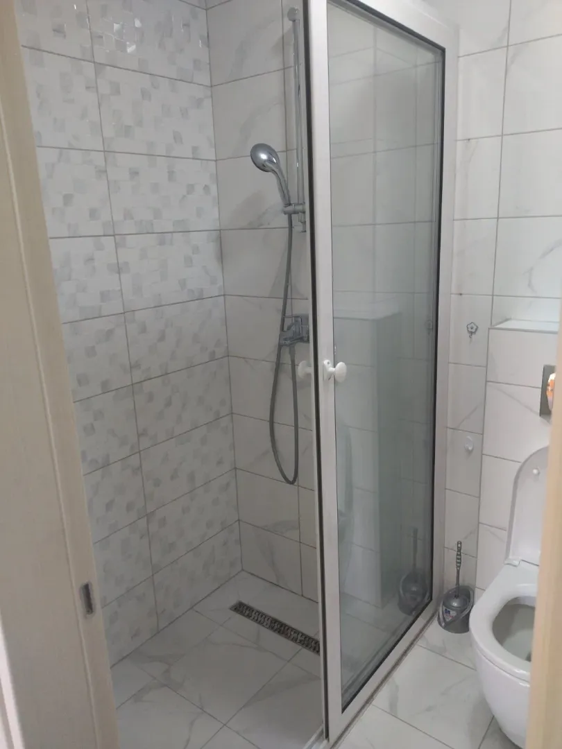 Moderne kupatilo sa tuš kabinom i bijelim pločicama.