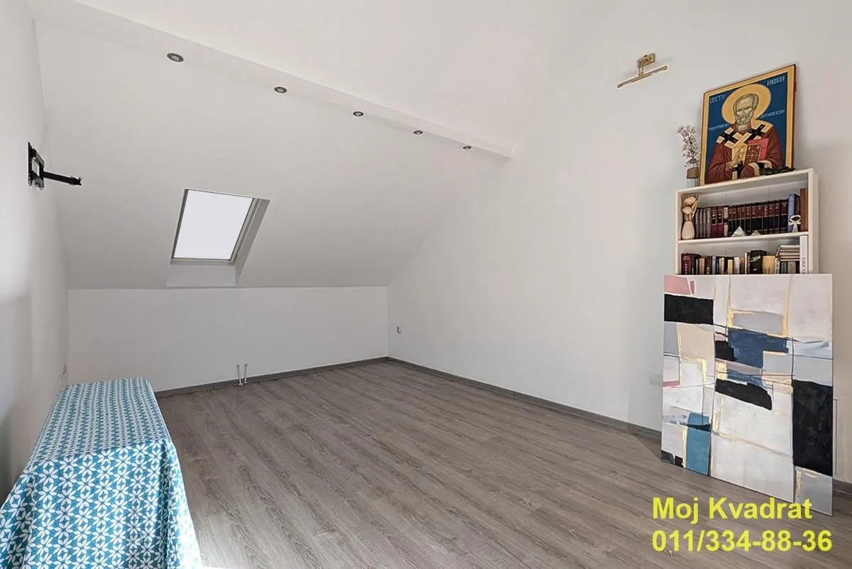 Empty attic room with wooden flooring, white walls, and a skylight.