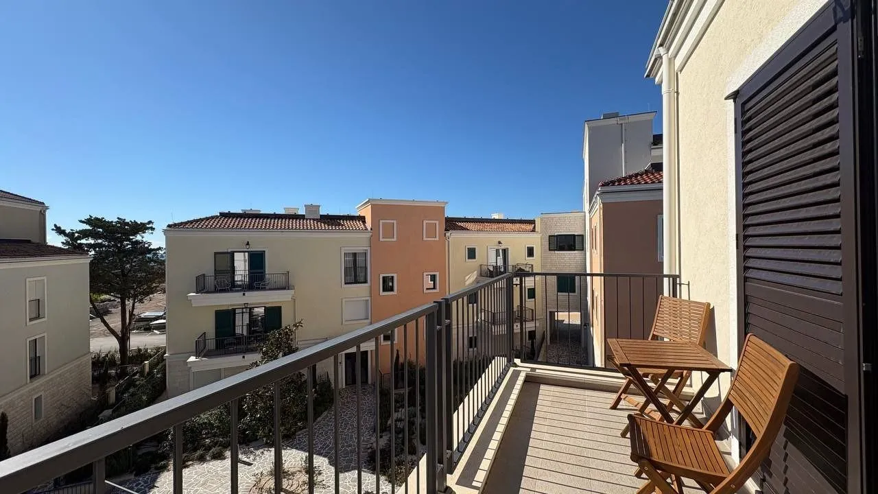 Manji namješteni balkon sa drvenim stolom i stolicama i pogledom na naselje.