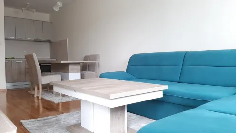 Svijetla dnevna soba sa plavom ugaonom garniturom i kuhinjom u pozadini. - image 10