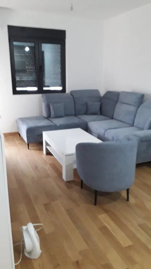 Svijetla dnevna soba sa sivom ugaonom garniturom i bijelim klub stolom.