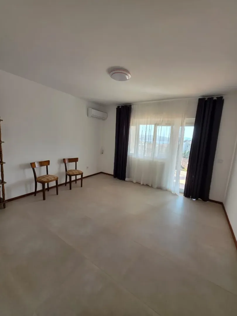 Prazna dnevna soba sa pločicama na podu i izlazom na terasu.