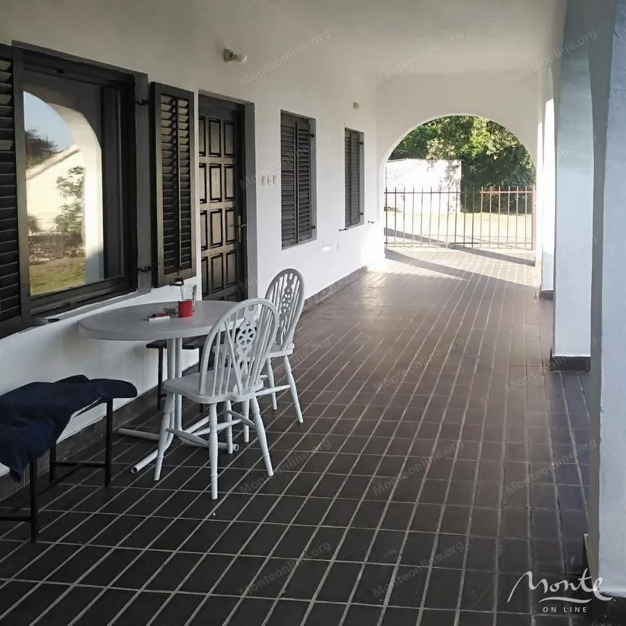 Covered terrace with a table and chairs in front of the house entrance.