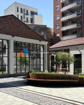 Pogled na spoljašnji prostor sa popločanim dvorištem, klupom i okolnim zgradama. - image 7