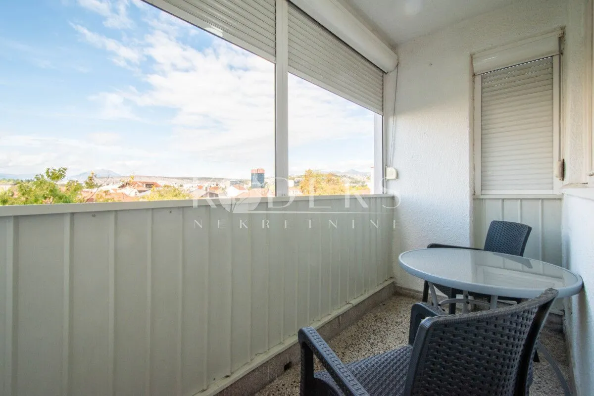 Enclosed balcony with seating furniture and a city view.