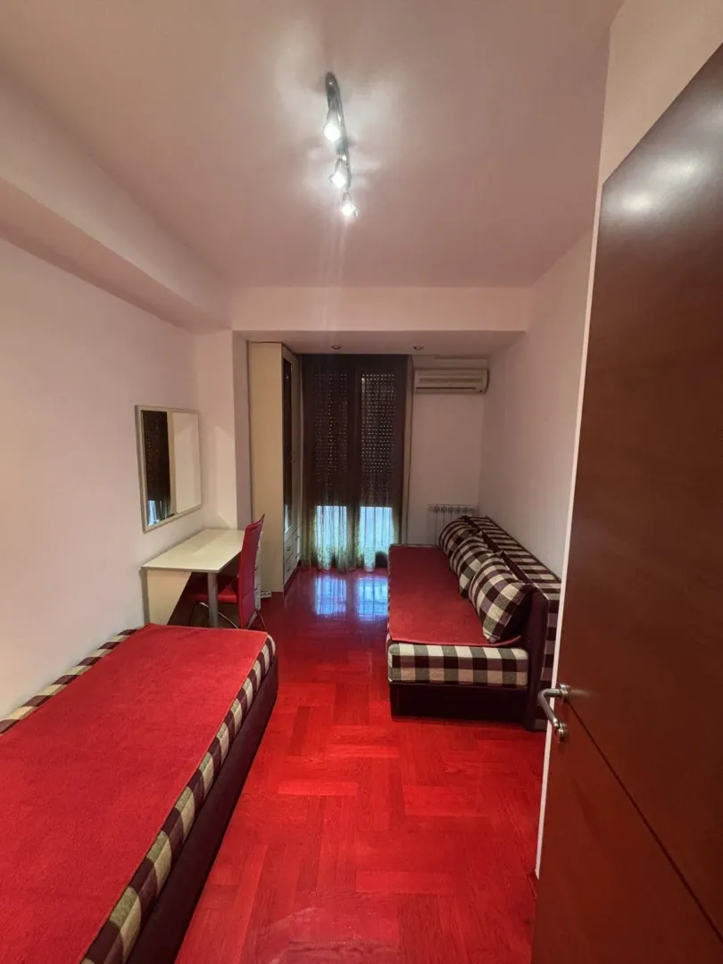 Simple bedroom featuring a red floor, a bed, and a study desk.