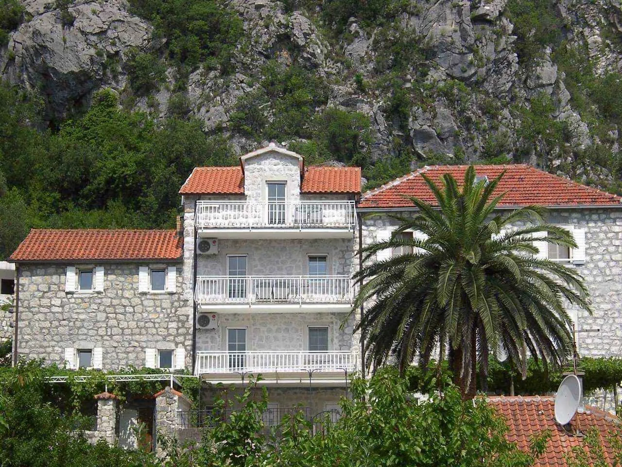 Spoljašnji izgled kamene kuće sa terasama i palmom u dvorištu.