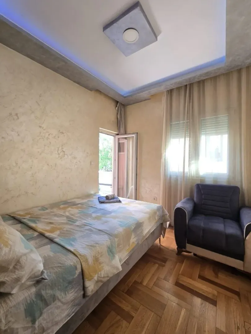 Namještena spavaća soba sa krevetom, foteljom i izlazom na terasu.