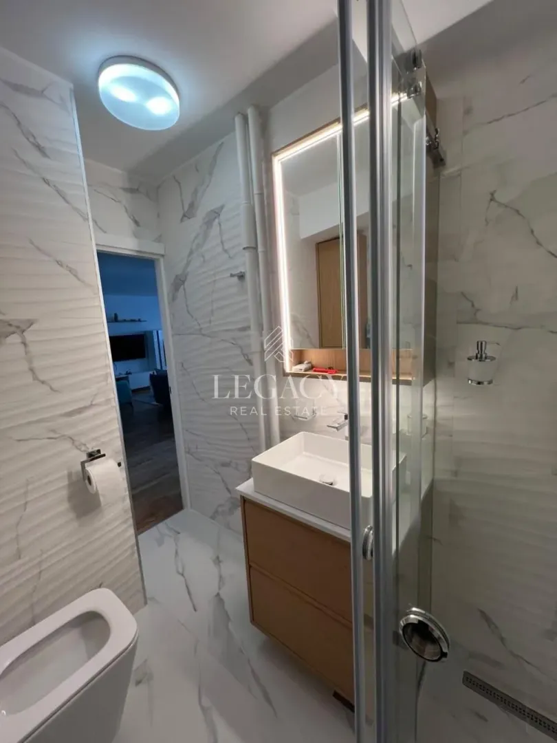 Modern bathroom equipped with a shower cabin, washbasin, and marble tiles.