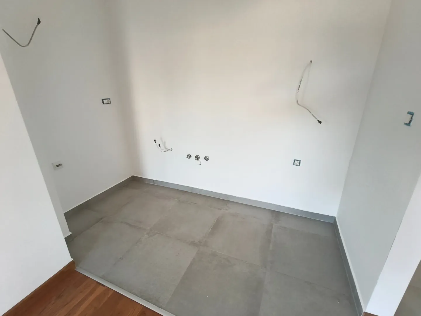 Prazna prostorija sa pločicama na podu i pripremljenim instalacijama.