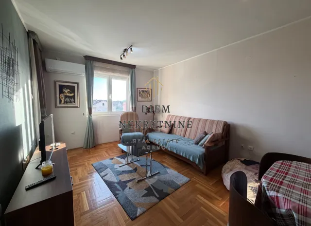 Dnevna soba sa garniturom, TV-om i trpezarijskim stolom.