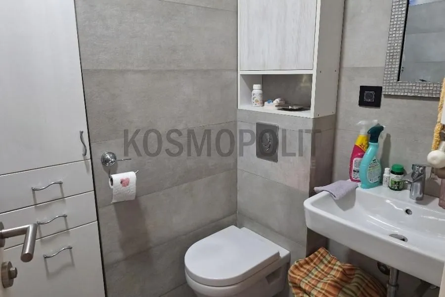 Manje kupatilo sa WC šoljom, umivaonikom i ugrađenim elementima za odlaganje.