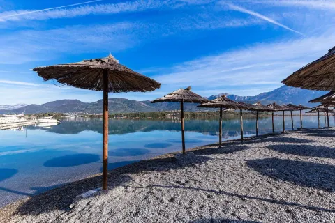Plaža sa slamnatim suncobranima pored mora sa pogledom na planine. - image 8