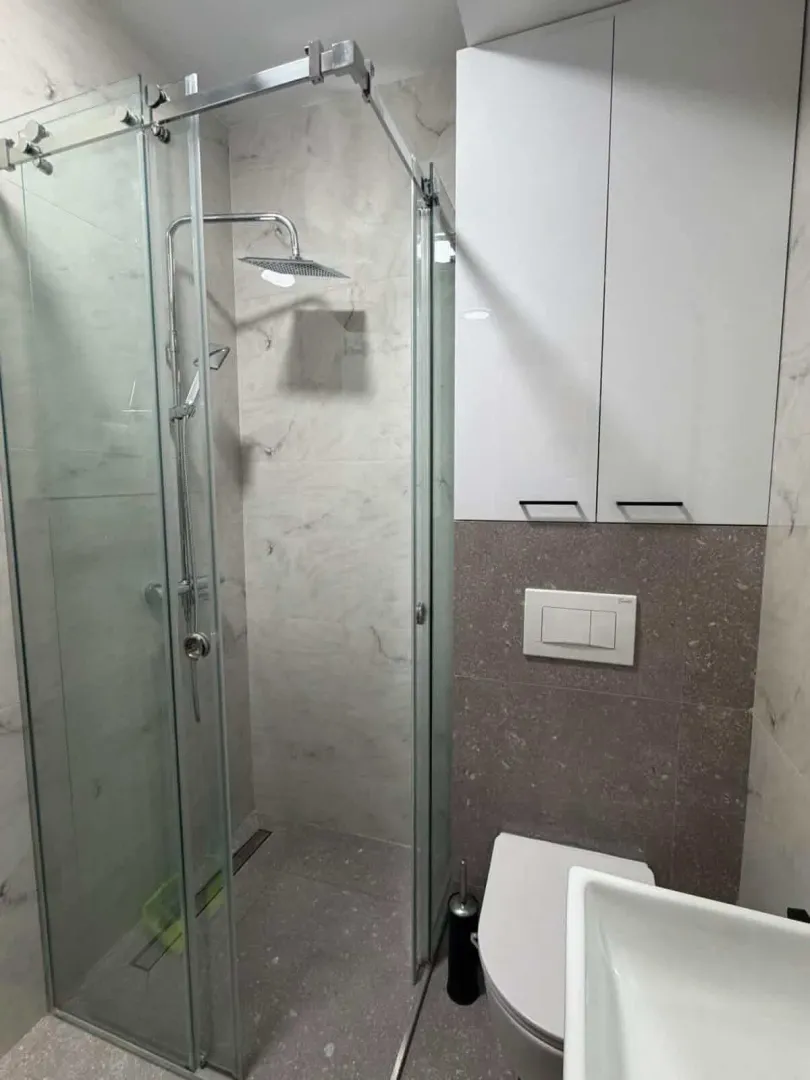 Moderne kupatilo sa tuš kabinom i bijelim visećim ormarićem.
