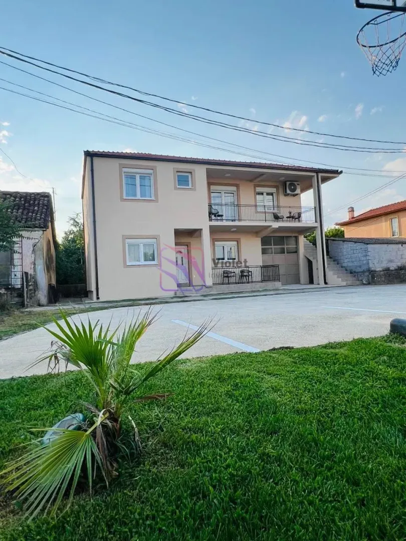 Pogled na dvospratnu kuću sa dvorištem i terasom.