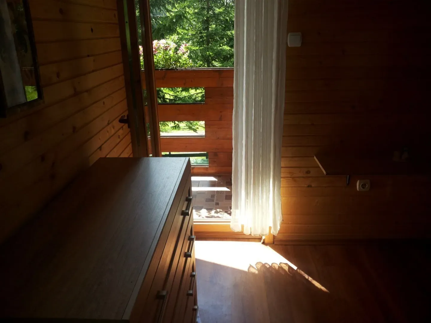 Drvena soba sa komodom i izlazom na balkon.