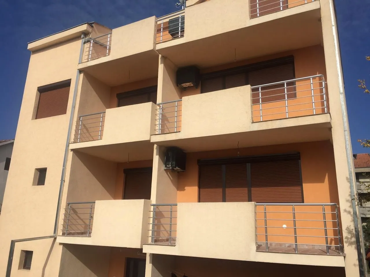Exterior of a multi-story residential building featuring spacious terraces and an orange facade.