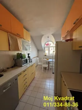 Dugačka kuhinja sa narandžastim i žutim elementima i trpezarijskim delom na kraju. - image 2