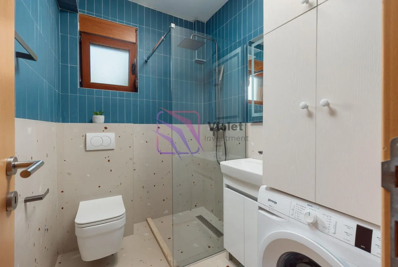 Moderne kupatilo sa tuš kabinom, wc šoljom, umivaonikom i veš mašinom.