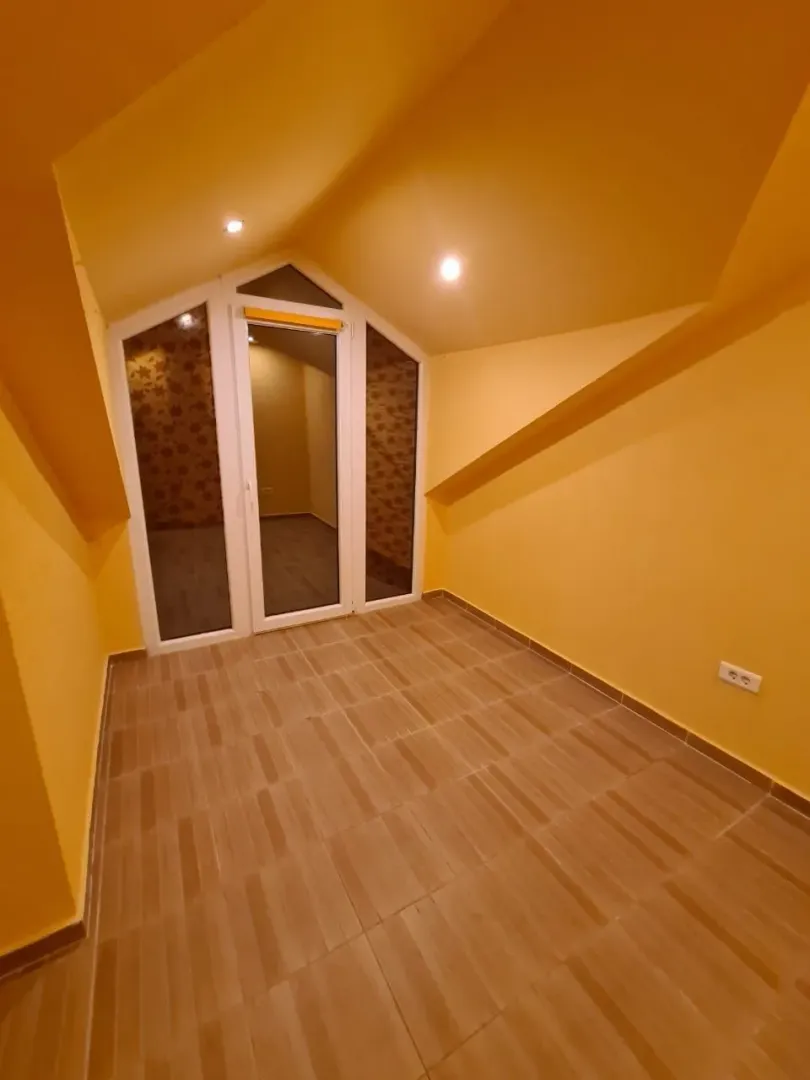Prazna potkrovna prostorija sa žutim zidovima i pločicama na podu.