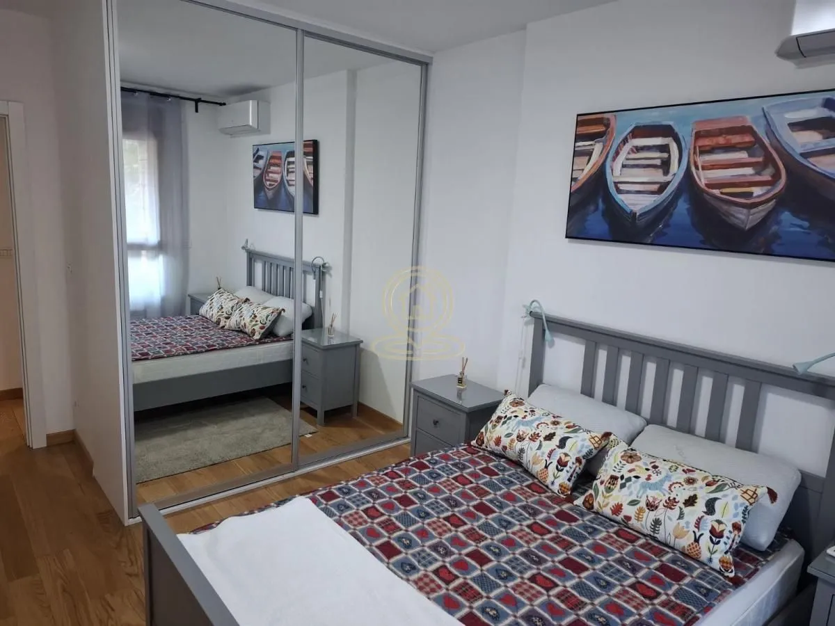 Nameštena spavaća soba sa bračnim krevetom, noćnim stočićem i velikim ogledalom na ormaru.