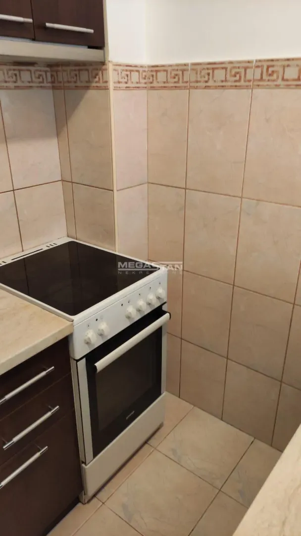 Deo kuhinje sa šporetom i keramičkim pločicama na zidu.