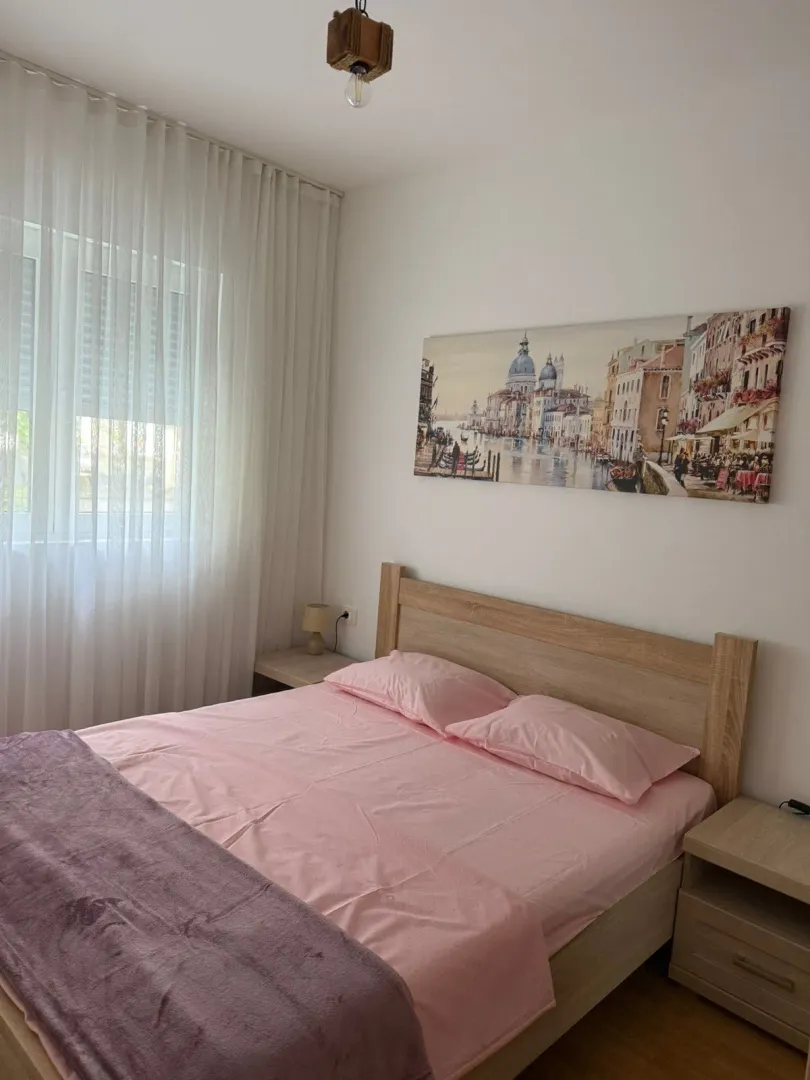 Spavaća soba sa bračnim krevetom, noćnim stočićima i velikim prozorom.