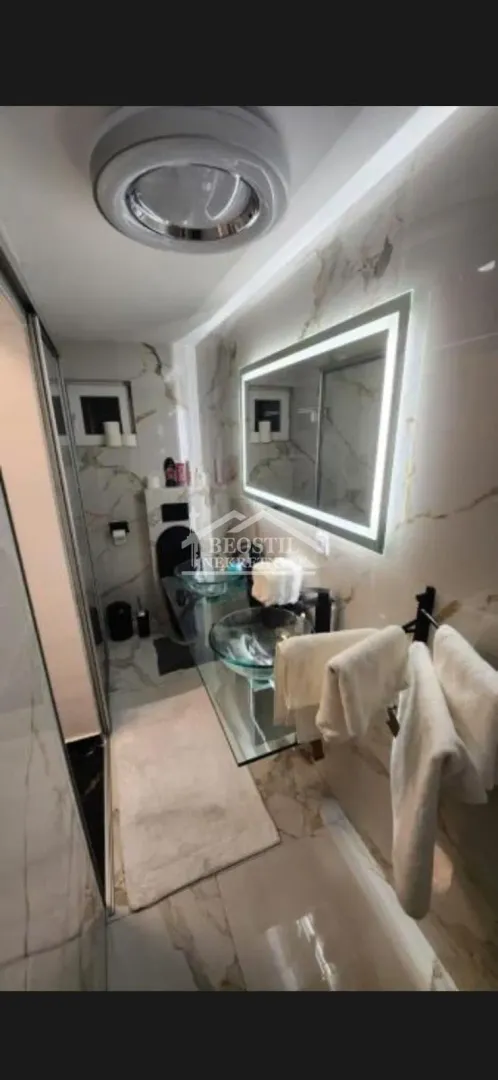 Modernly equipped bathroom with a washbasin, backlit mirror, and a walk-in shower.
