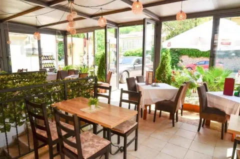 Natkrivena zastakljena terasa restorana sa stolovima i stolicama. - image 10