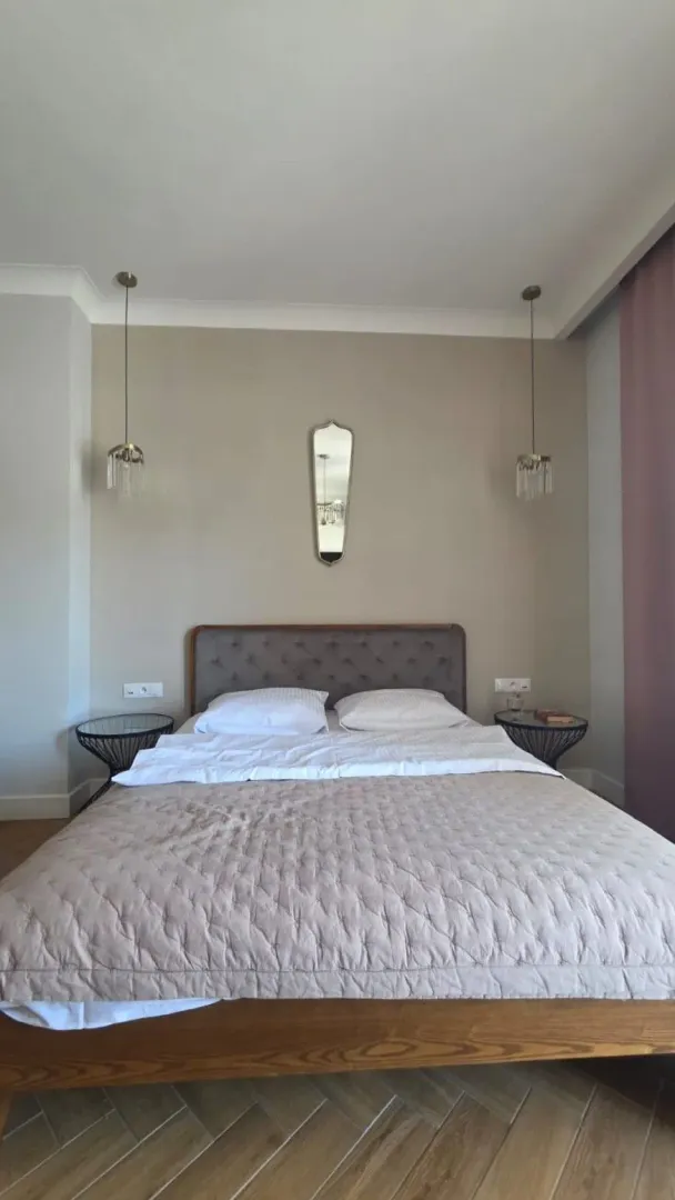 Uređena spavaća soba sa bračnim krevetom, noćnim stočićima i visećim lampama.