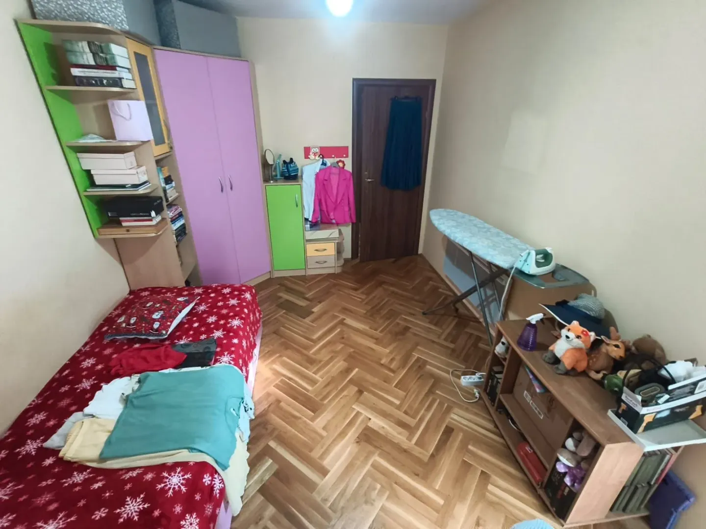 Manja spavaća soba sa krevetom, ormarima i daskom za peglanje.