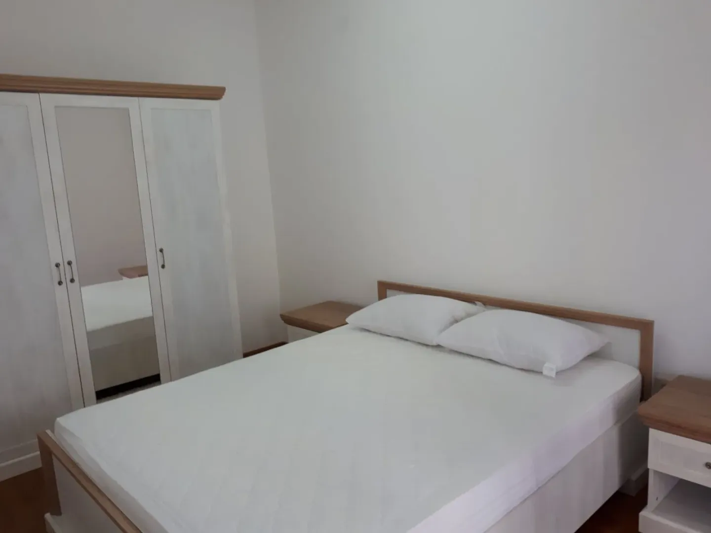 Svjetla spavaća soba sa bračnim krevetom, bijelim ormarom i noćnim stočićima.
