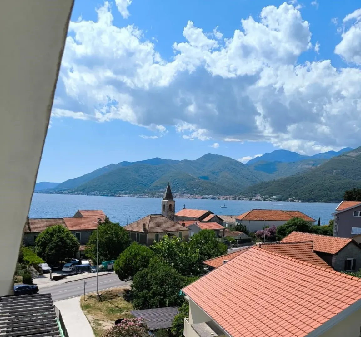 Pogled sa terase na more, krovove kuća i planine.