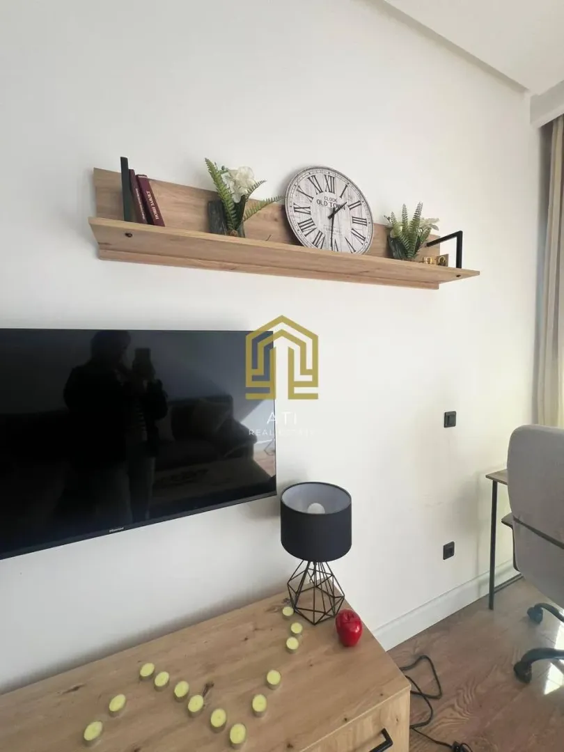Dnevna soba sa TV-om, policom i ukrasnim detaljima.
