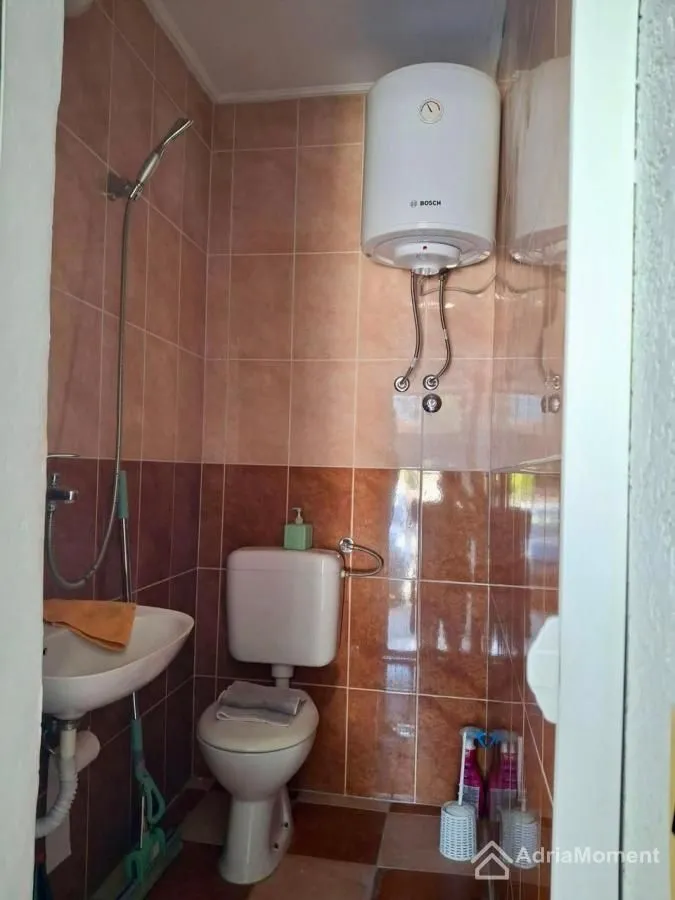 Smaller bathroom with a shower, toilet bowl and water heater.