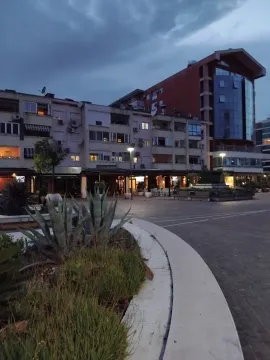 Pogled na stambenu zgradu i popločani trg sa zelenilom u sumrak. - image 10