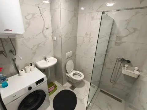 A modern bathroom equipped with a walk-in shower, washbasin, and washing machine. - image 9