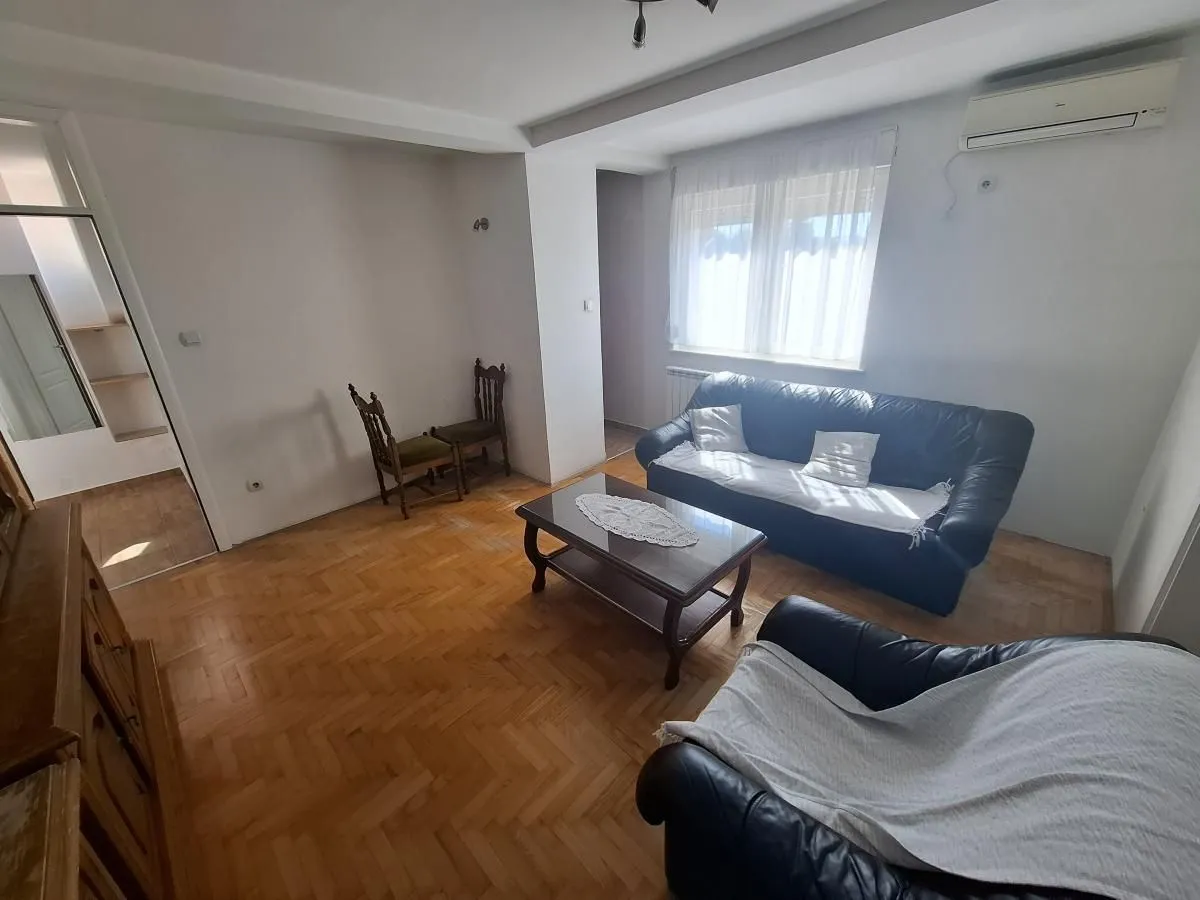 Dnevna soba sa garniturom za sedenje, stočićem i parketom na podu.