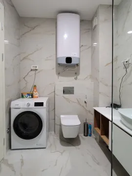 Modernly equipped bathroom with a washing machine, toilet, and water heater. - image 10