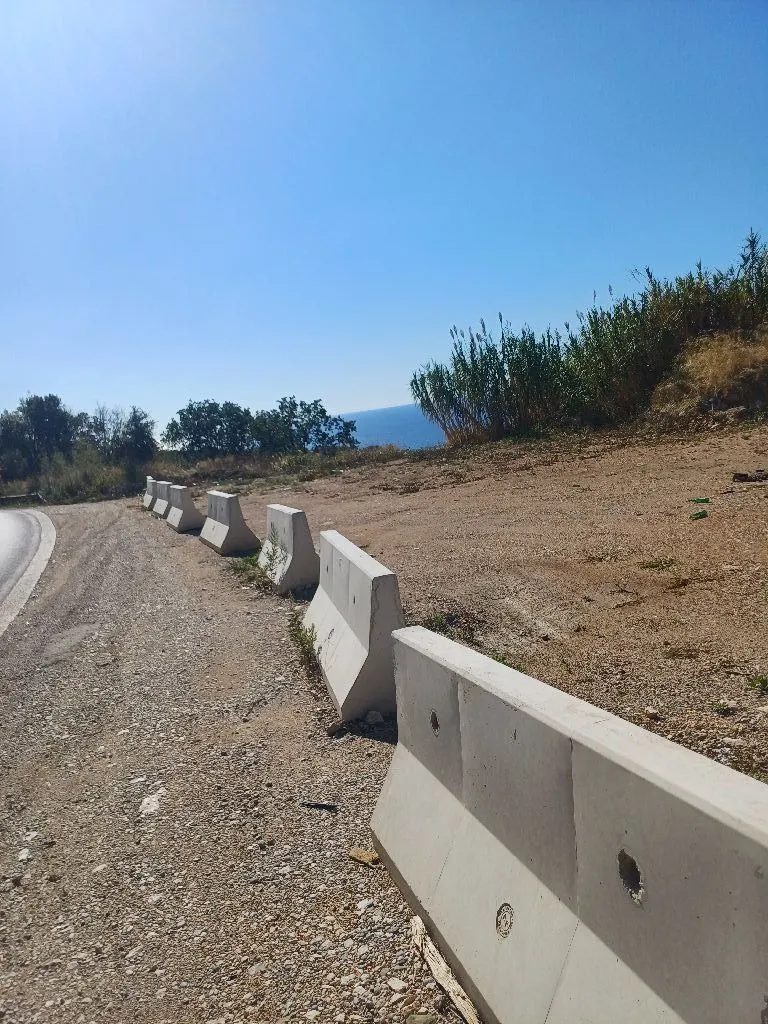Pogled na plac sa betonskim barijerama pored puta i pogledom na more.
