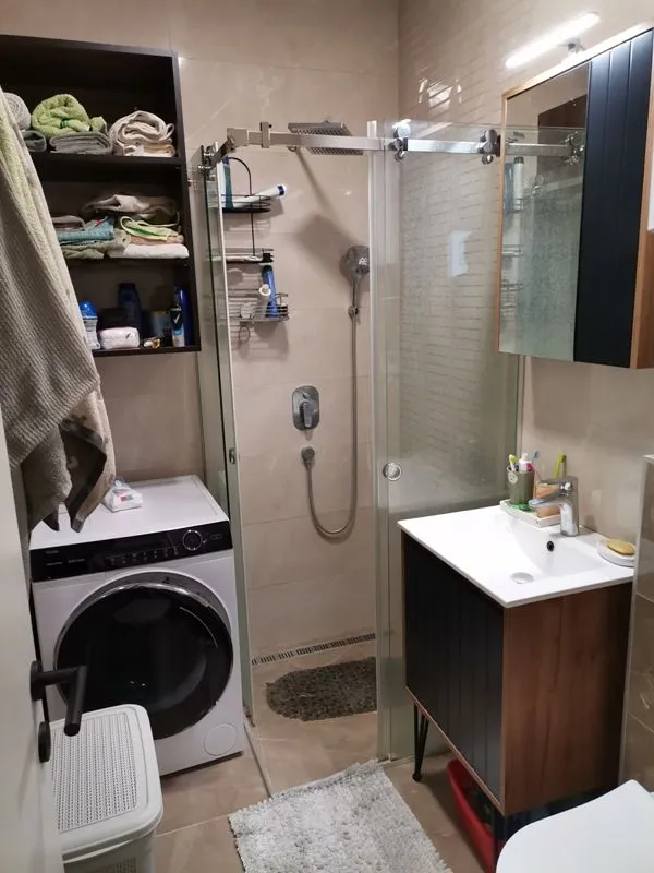 Kupatilo sa tuš kabinom, umivaonikom, ogledalom i veš mašinom.